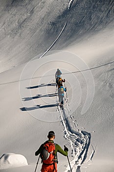 Ski tour group of people walking on deep white powdery snow path of snow-capped mountain