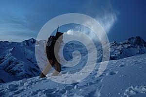 Ski touring man commit climb on night winter mountain. Tourist with headlamp, backpack and a snowboard behind his back walking on photo
