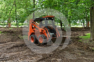 Skid steer loader clearing the site in public park moving soil and performing landscaping works for the territory improvement