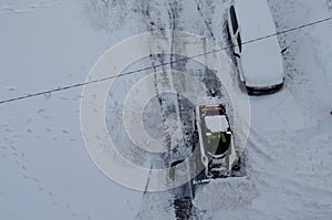 Skid steer loader removes snow from the city streets. Top view of the road with cars and snow blower. Seasonal work in winter