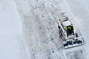 Skid steer loader removes snow from the city streets. Top view of the road with cars and snow blower. Seasonal work in winter