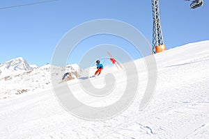 Skier in blue jacket, black helmet and orange pants on the piste slope in winter with snow mountains in Alps