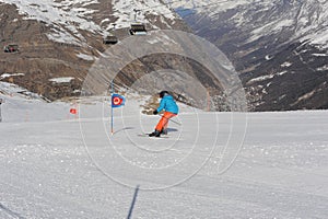 Skier in blue jacket, black helmet and orange pants on the piste slope in winter with snow mountains in Alps