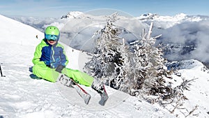 Skier boy sit on top of the mountain in clouds lift hands up