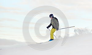 Skier descending from snow-covered high mountain top. Extreme skiing concept. Mountains view. Winter sky on background.