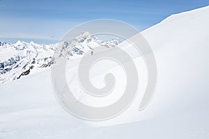 Skier in the distance across large cornice of windblown snow. Above him is Mount Sir Donald in Glacier National Park, Canada