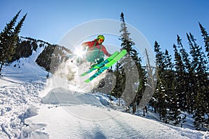 Skier freerider jumping from a snow ramp in the sun on a background of forest and mountains
