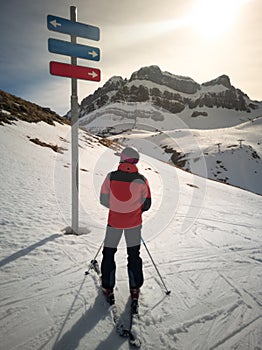 Skier in front of a ski resort signpost doubting which ski slope to go to