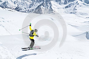 A skier in full sports equipment jumps into the precipice from the top of the glacier against the background of the blue