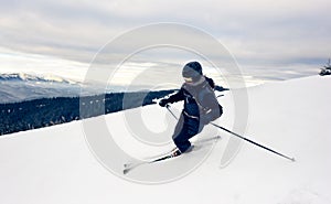 Skier inclining turning on snow-capped mountain peak. Extreme skiing concept. Mountains view. Grey sky on background.