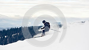 Skier inclining turning on snow-capped mountain peak. Extreme skiing concept. Mountains view. Grey sky on background.