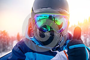 Skier man in balaclava, helmet and glasses is taking selfie in snow on mountain ski lift, sun light
