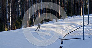 Skier man is skiing riding fast downhill on ski slope in forest among trees.