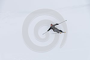 skier on the piste, going down the slope among the Alpine mountains, which are not visible due to cloudiness