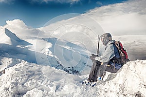 Skier sits with skis on big rock on mountains backdrop. Bansko, Bulgaria