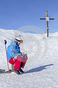 The skier sitting on a bench a snowy slope and looking at the smartphone and around landscape of snowy Alps