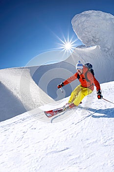 Skier skiing downhill in high mountains against blue sky