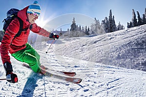 Skier skiing downhill in high mountains against against the fairytale winter forest with sunset