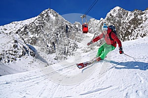 Skier skiing downhill in high mountains against cable lift