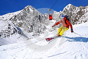 Skier skiing downhill in high mountains against cable lift