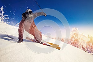 Skier skiing downhill during sunny day in mountains and forest. Extreme winter sports