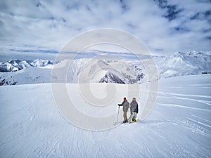 Skier and snowboarder standing on mountain top against blue sky and mountains panorama. Two active friends have vacation