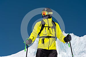 Skier standing on a slope. Man in a light suit, the helmet and mask in skiing is to ski. In the background snow-capped