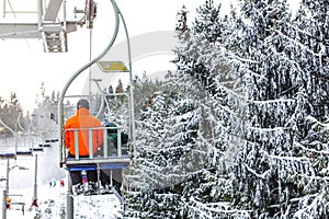 Skiers on chair lift, piste under, snow covered trees on right side