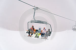 Skiers in colorful ski suits on skis with poles ride on a four-seater chairlift up the slope