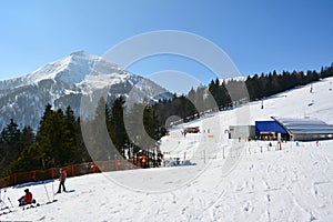 Skiers go down a ski track at a ski resort against the background of mountains and forest trees