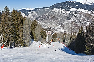 Skiers on piste through trees in alpine resort