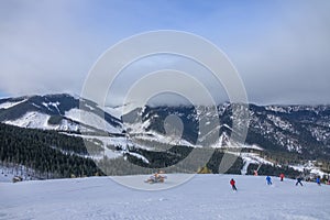 Skiers and a Rescue Snowmobile Against the Backdrop of Mountain Peaks Hidden by a Low Cloud