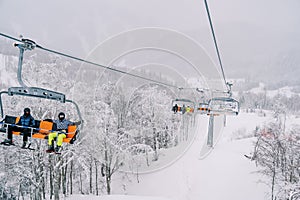 Skiers ride a four-seater chairlift over a snowy forest up the mountain