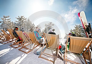 Skiers sitting with deck chairs in winter mountains. Back view photo
