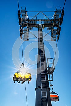 Skiers sitting at ski-lift chair and cable car mast