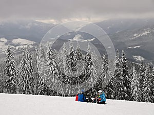 Skiers in ski suits are sitting on the snow. resting on the top of the mountain