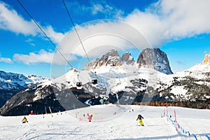 Skiers skiing down the slope in ski resort in winter Dolomites. Val Di Fassa, Italy