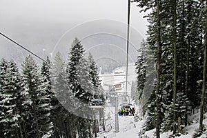 Skiers and snowboarders climb up the slope on a six-seater chair lift in the snow-covered forest