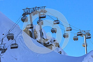 Skiers and snowboarders ride on chair ski lift at Gorky Gorod mountain ski resort in Sochi, Russia, against blue sky in the evenin