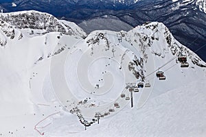 Skiers and snowboarders ride on ski lift on winter day. Ski slopes and tracks in Gorky Gorod mountain resort host ski and