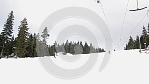 Skiers using ski lift anchor on the mountain. People moving slowly uphill on drag lift on snow covered landscape. Winter sports, s