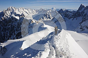 Skiers walking on mountain ridge covered with snow in French Alps in winter with beautiful panorama and blue sky