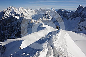 Skiers walking on mountain ridge covered with snow in French Alps in winter with beautiful panorama and blue sky