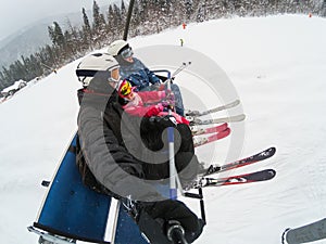 Skiing, ski lift, ski resort - happy smiling family skiers on ski lift making selfie