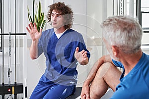 Skilful physical therapist giving instructions while chatting with his retirement client