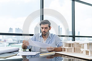 Skilled architect engineer holding blueprint on desk in modern office. Tracery.