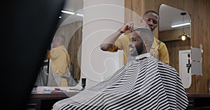 Skilled barber working with male client cutting hair with scissors indoors in salon