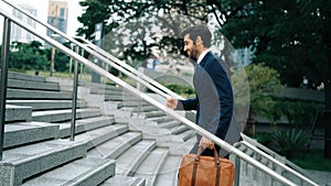 Skilled business man walking up stair while holding bag in the hand. Exultant.