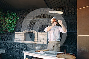 Skilled chef preparing dough for pizza rolling with hands and throwing up.