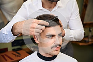 Skilled coiffeur combing client& x27;s hair after cutting in barbershop photo